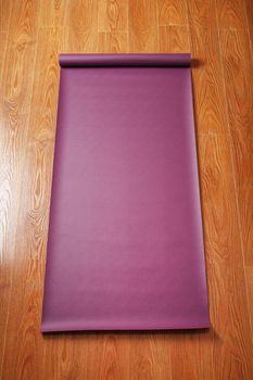 A lilac-colored yoga mat is spread out on the wooden floor with a Ganapati figurine. Top view