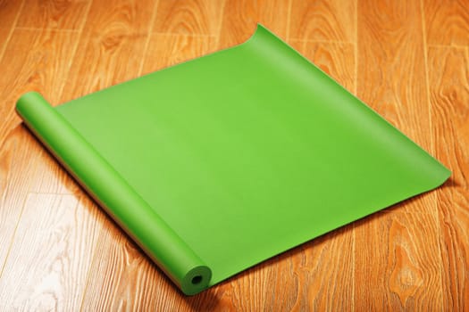 A green yoga mat is laid out in a roll on the wooden floor. A healthy lifestyle in isolation.