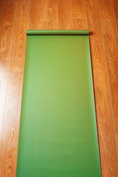 Green Yoga mat on wooden floor unfolded. Healthy lifestyle, fitness, sports. Top view.