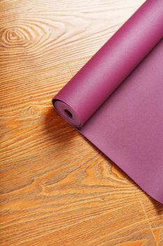 A lilac yoga mat is twisted on the wooden floor. Healthy lifestyle, sports
