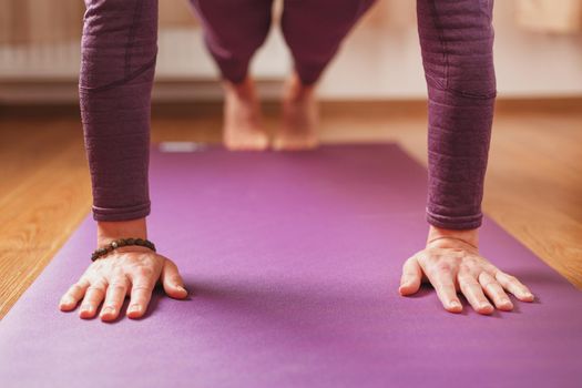 A girl does yoga asanas on a lilac rug in the living room.