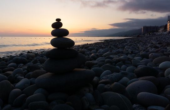 Stack of gray zen stones on the beach at sunset, beautiful seascape. Made of stone tower as rest balance vacation concept.