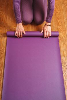 A man lays out a lilac yoga mat on the wooden floor of a house.