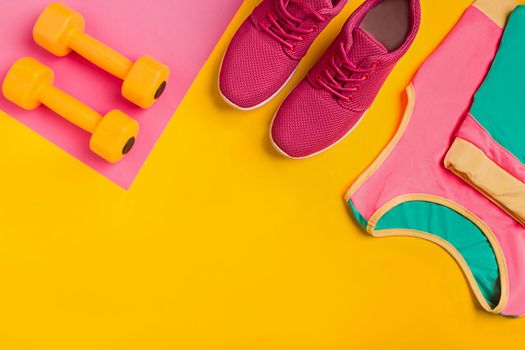 Athlete's set with female clothing, dumbbells and bottle of water on yellow background. Top view. Still life