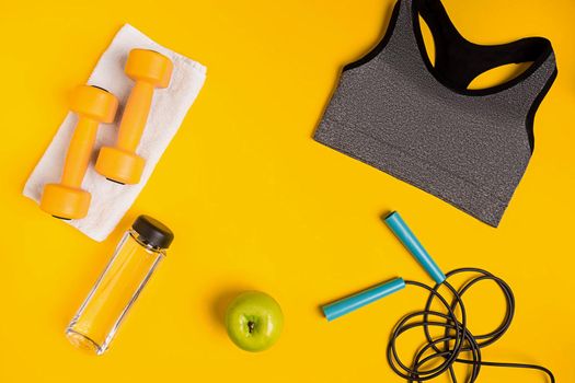 Athlete's set with female clothing, dumbbells and bottle of water on yellow background. Top view. Still life