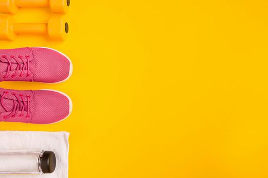 Athlete's set with female clothing, dumbbells and bottle of water on yellow background. Top view. Still life