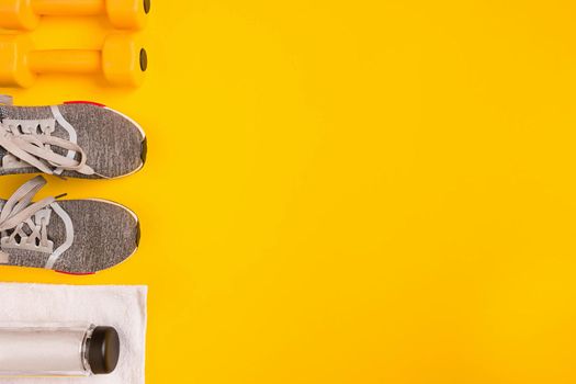 Athlete's set with female clothing, dumbbells and bottle of water on yellow background. Top view. Still life