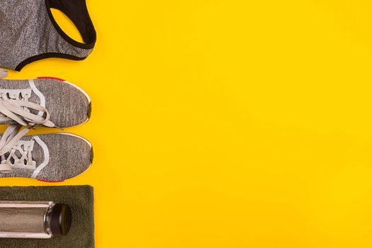 Athlete's set with female clothing, dumbbells and bottle of water on yellow background. Top view. Still life