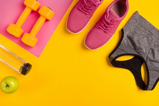 Athlete's set with female clothing, dumbbells and bottle of water on yellow background. Top view. Still life