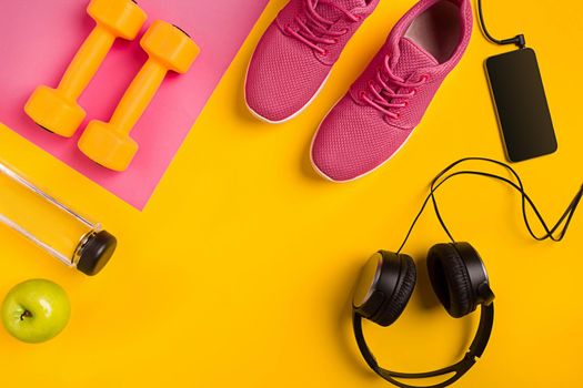 Athlete's set with female clothing, dumbbells and bottle of water on yellow background. Top view. Still life