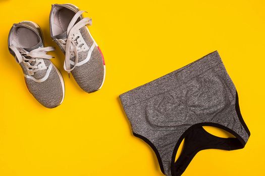 sport, fitness, healthy lifestyle, cardio training and objects concept - close up of female sports clothing and sneakers on a yellow background. Top view. Still life. Copy space