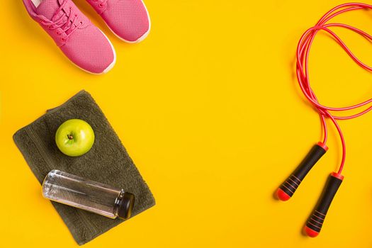 Athlete's set with female clothing, skipping rope and bottle of water on yellow background. Top view. Still life