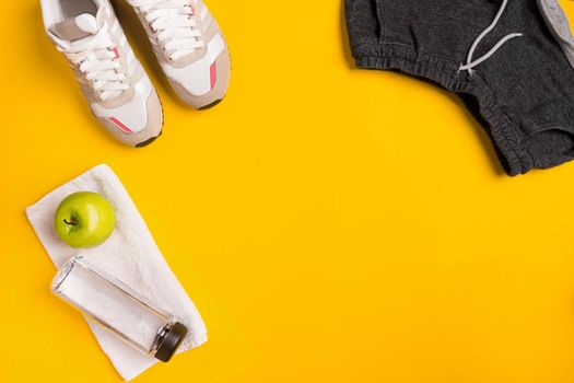 Athlete's set with female clothing and bottle of water on yellow background. Top view. Still life