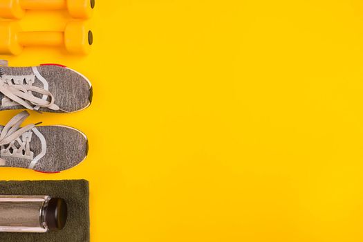 Athlete's set with female clothing, dumbbells and bottle of water on yellow background. Top view. Still life