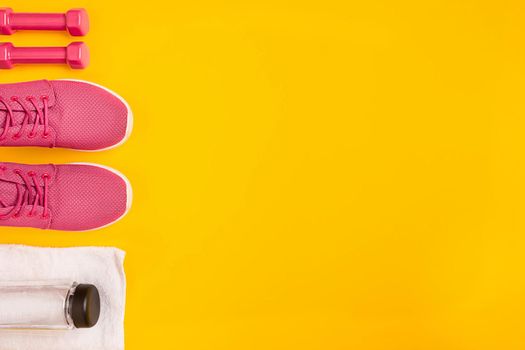 Athlete's set with female clothing, dumbbells and bottle of water on yellow background. Top view. Still life