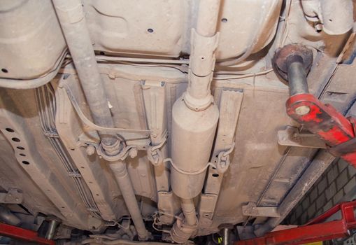 Bottom view of the underbody of an old car on a lift. In the garage, a man changes parts on a vehicle. Small business concept, car repair and maintenance service. UHD 4K.