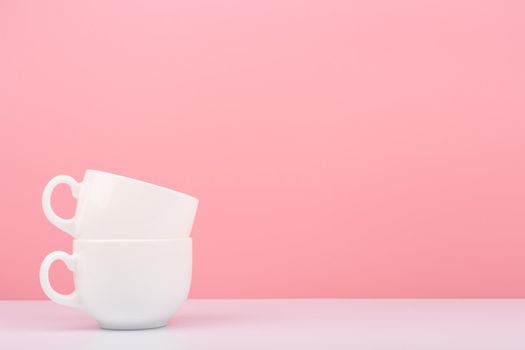 Close up of white ceramic cup in another against pink background with copy space. Concept of hot drinks and kitchenware