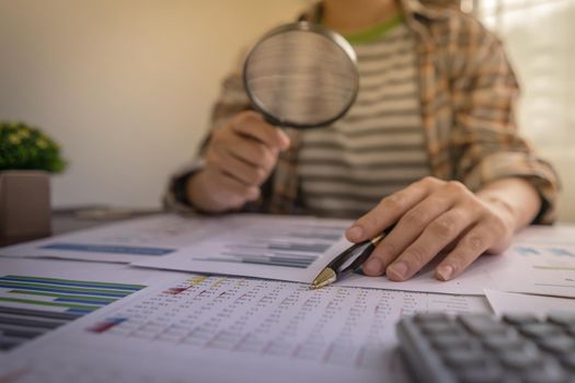 Businesswomen using magnifying to review balance sheet reports. Internal audit, Analyze return on investment, Auditing tax Concept.