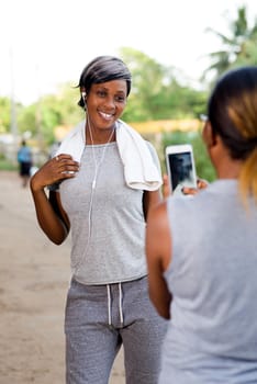 young woman standing photographing her friend after sport with mobile phone.