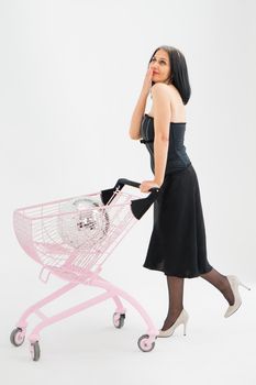 Studio photo of middle aged woman starting getting grey-haired wearing black clothes with silver disco ball in shopping basket white background, middle age sexy lady, happy life concept.