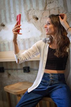 Female portrait of young active girl in white shirt taking a photo of herself indoors on loft wall background, selfie time, happy people concept