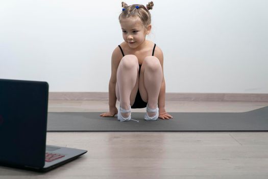 kid girl in a gymnastic leotard is engaged in classical dances with a trainer online.