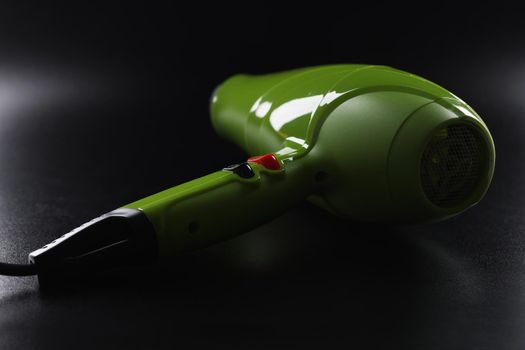 Close-up of green professional hairdryer device lay on black background, tool for beauty master. Equipment make hot air and dry hair. Beauty salon concept