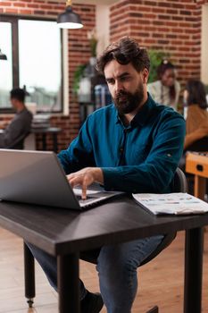 Busy businessman analyzing company statistics typing marketing strategy planning business collaboration. Entrepreneur man brainstorming ideas while working at brick wall startup office