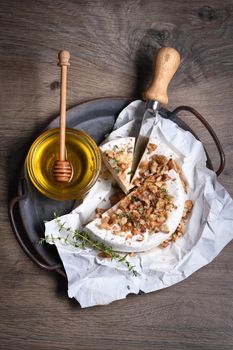 Camembert soft cheese is served on an iron dish with walnuts, honey and thyme. View from above