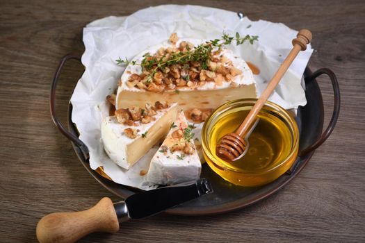 Camembert soft cheese is served on an iron dish with walnuts, honey and thyme. 