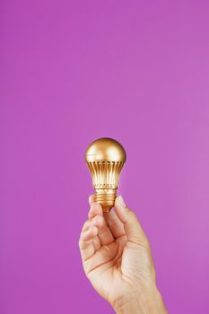Gold light bulb as an idea in a female hand on a pink background. Isolate