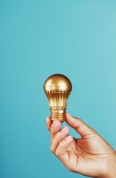 Gold light bulb in hand on a blue background, as a concept of ideas and assistance. Isolate, minimalistic