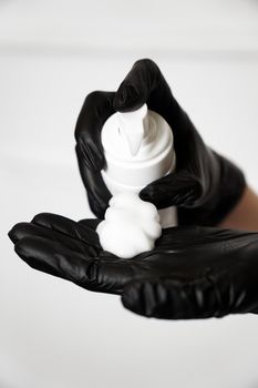 Closeup of a female hand with foam on the palm in black gloves. Woman squeezes foam onto her hand. Cosmetic procedures and products, skin care