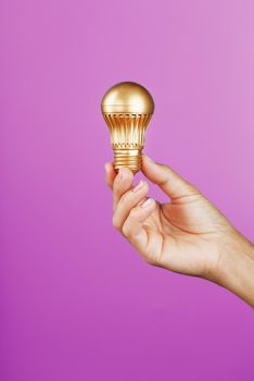 Gold light bulb as an idea in a female hand on a pink background. Isolate