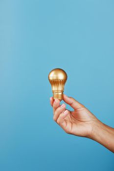 Gold light bulb as an idea in a female hand on a blue background. Isolate