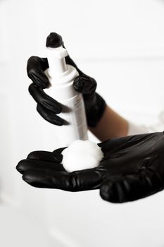 Closeup of a female hand with foam on the palm in black gloves. Woman squeezes foam onto her hand. Cosmetic procedures and products, skin care