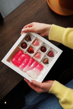 Hands of a young woman holding a gift with sweets. Closeup of a box of handmade candies in hands. Sweet Valentine's Day Gift. Women's Day.