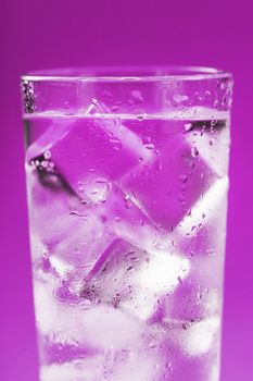 A glass with ice water and ice cubes on a blue background. A refreshing and chilling drink in hot weather.