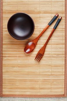 Natural wood plate, spoon and fork on a bamboo backing. Asian food handicraft concept. View from above