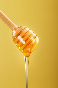Honey drips in a thin stream from a honey dipper on a yellow background. Healthy food diet concept, ecologically pure product