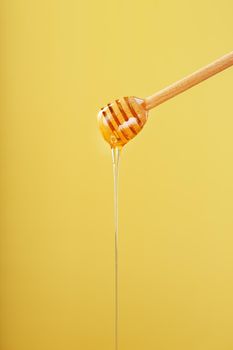 Honey flows down from a honey bucket on a yellow background. The concept of healthy and eco-friendly nutrition