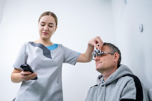 Examining patient vision. Eye exam. Optometrist checking patient eyesight and vision correction. Patient undergoing vision check with special ophthalmic glasses at eye clinic. Selection of eyeglasses.