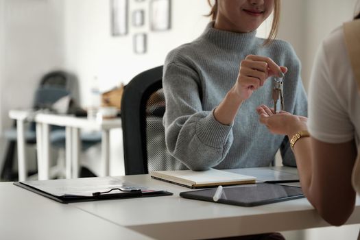 real estate agent holding house key to his client after signing contract agreement in office,concept for real estate, moving home or renting property.