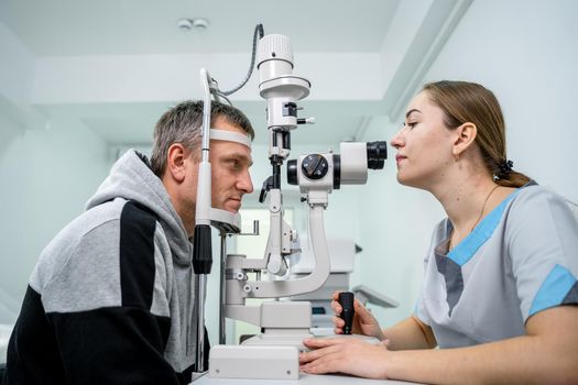 Ophthalmologist and patient testing eyesight. Man doing eye test with optometrist. Ophthalmologist using apparatus for eye examination in clinic. Doctor examining patient doing eyesight measurement.