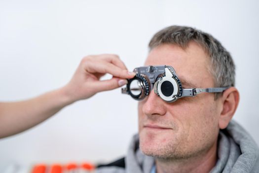 Male patient undergoes an eye test and prescription for eyeglasses in ophthalmology clinic. Optometrist checking patient eyesight and vision correction. Changing lenses on trial frame on patient nose.