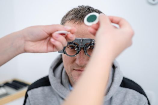 Vision correction. Selection of eyeglasses. Professional trial frames on male patient face while doctor checks eyesight in modern ophthalmologist office. Optometrist checking prescription for glasses.