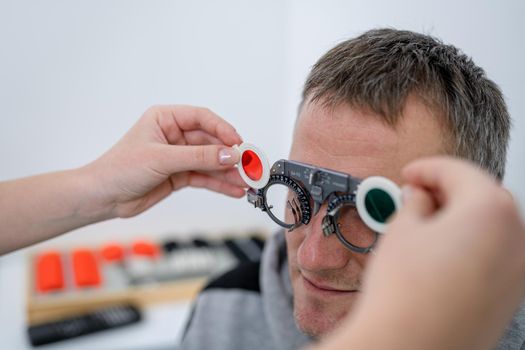 Vision correction. Selection of eyeglasses. Professional trial frames on male patient face while doctor checks eyesight in modern ophthalmologist office. Optometrist checking prescription for glasses.