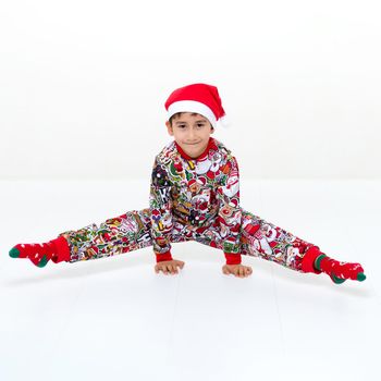 A boy in a Christmas outfit does a handstand and sits on the twine. Gymnast in bright colorful overalls, socks and santa claus hat performing rhythmic gymnastic exercises over isolated white background