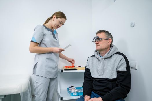 Male patient undergoes an eye test and prescription for eyeglasses in ophthalmology clinic. Optometrist checking patient eyesight and vision correction. Changing lenses on trial frame on patient nose.