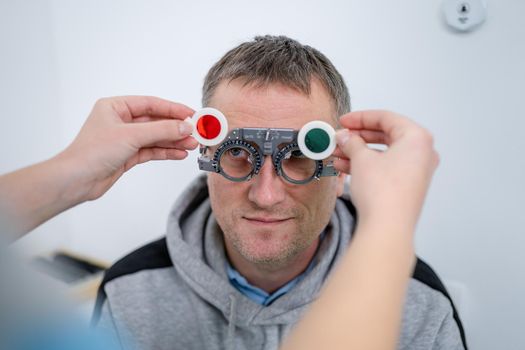 Vision correction. Selection of eyeglasses. Professional trial frames on male patient face while doctor checks eyesight in modern ophthalmologist office. Optometrist checking prescription for glasses.